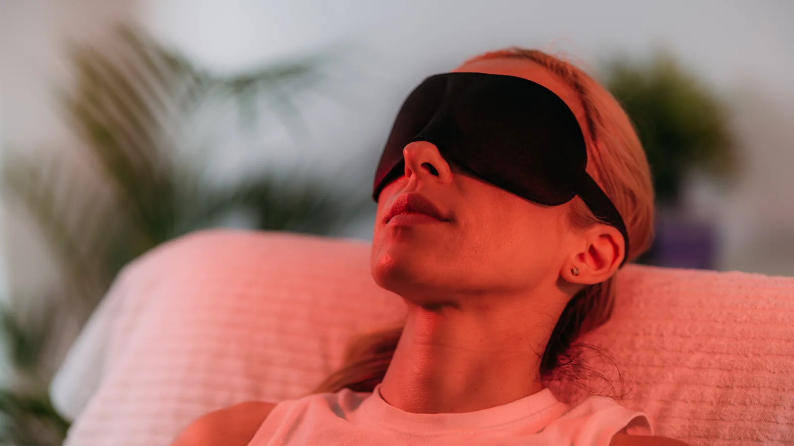 A woman lying back with an eye mask on, bathed in warm red light during a home therapy session.